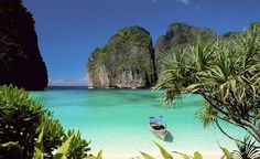 a small boat in the clear blue water next to two large rock formations and palm trees