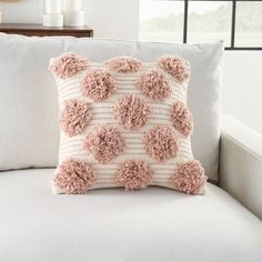 a pillow with pom - poms on it sitting on a couch in front of a window