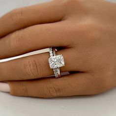 a woman's hand with a diamond ring on top of her finger and the other hand holding an engagement ring