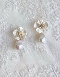 two white flowers and pearls are on top of a lace tablecloth, next to a pair of earrings