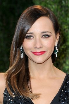 a woman in a black dress with red lipstick and earrings on her face smiling at the camera