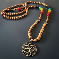 The Chakra Colors Yoga Mala Beaded Necklace is a spiritual and meaningful piece of handmade jewelry that combines natural elements and powerful symbolism. This unique necklace is commonly used in meditation and yoga practices to enhance the spiritual experience and promote a sense of balance and harmony.The handmade necklace is made with natural sandalwood beads, which are known for their calming and soothing properties. Sandalwood has been used for centuries in various spiritual practices to he Holistic Necklaces With Wooden Beads For Festivals, Holistic Wooden Beads Necklace As A Gift, Holistic Style Necklace With Wooden Beads, Wooden Beads Amulet Jewelry For Festival, Holistic Festival Necklaces With Wooden Beads, Holistic Style Necklace With Wooden Beads For Gifts, Holistic Wooden Beads Necklace For Gift, Amulet Style Jewelry With Wooden Beads For Festival, Holistic Style Wooden Beads Necklace For Gifts