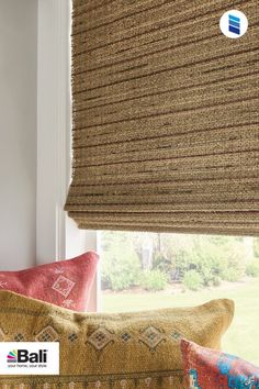 an image of a window with roman blinds in the windowsill and pillows on the couch