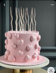 a pink cake with lots of hearts on it and candles sticking out of the top