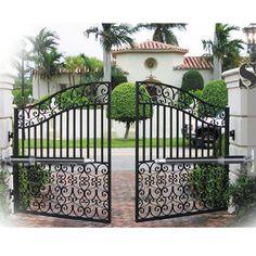 an iron gate is shown in front of a house with trees and bushes on either side