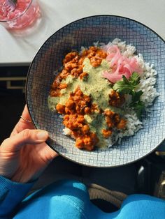 a person holding a plate with rice, meat and sauce on it in their hand