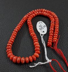 an orange beaded necklace with a white tag hanging from it's end on a black surface