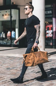 Man in a street wearing black clothes and holding a brown leather bag Mens Weekend Bag, Purse Outfit, Vintage Briefcase, Flight Bag, Leather Weekender Bag, Leather Weekender, Mens Travel Bag, Leather Duffle Bag, Travel Brand