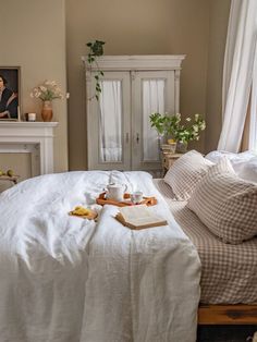 a bed with white sheets and pillows next to a fireplace in a room filled with furniture