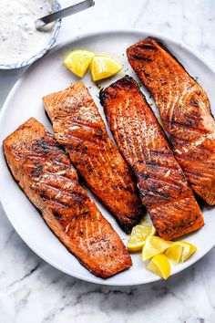 grilled salmon on a plate with lemon wedges and sour cream sauce in the background