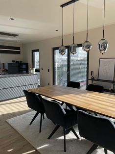 a dining room table with black chairs and lights hanging from the ceiling