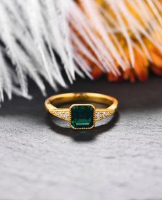 an emerald and diamond ring sitting on top of a white feathered tablecloth with feathers in the background