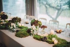 the table is covered with moss and lit candles for an elegant wedding reception or special event