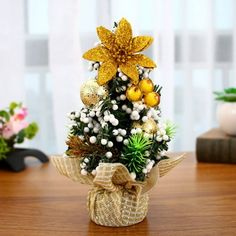 a small christmas tree decorated with gold and white ornaments on a wooden table in front of a window