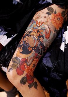 a woman's arm with tattoos on it and flowers in the middle, sitting on a chair