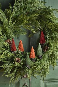 an evergreen wreath with cones and pine cones hanging from the front door, on a green door