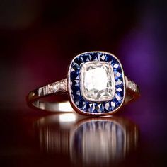 an antique diamond and blue sapphire ring on a reflective surface, with purple lighting in the background