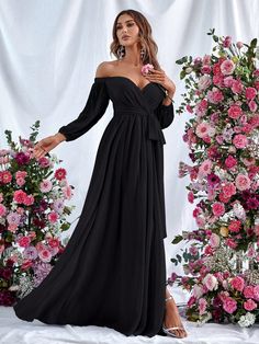 a woman standing in front of flowers wearing a black dress with off the shoulder sleeves