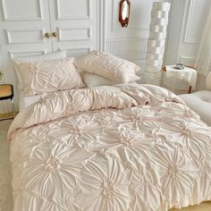 a white bed sitting in a bedroom next to a chair and table with pillows on top of it