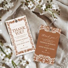 two tags with thank you written on them sitting next to some white and brown flowers