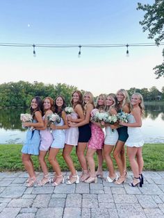 a group of women standing next to each other on a brick walkway near a body of water