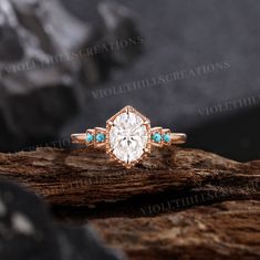 an engagement ring with turquoise stones on top of a tree branch in front of some rocks