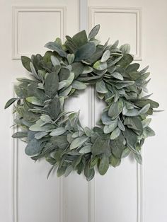 a wreath is hanging on the front door with green leaves and greenery around it