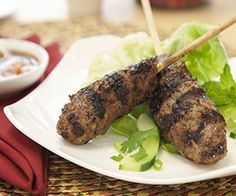 two grilled meats on skewers with lettuce and dipping sauce