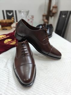 A chocolate brown classic Oxford shoe is a timeless and versatile footwear choice for both formal and semi-formal occasions.  It follows the classic Oxford shoe style, characterised by its closed lacing system, which gives it a sleek and formal appearance. The shoe has a plain, unadorned design, emphasizing its elegance. The upper of the shoe is made of high-quality, supple leather with a polished finish. This not only enhances the shoe's aesthetics but also adds to its durability and longevity. Classic Brown Closed Toe Lace-up Shoes, Brown Lace-up Derby Shoes For Business, Brown Closed Toe Business Oxfords, Classic Brown Semi-formal Oxfords, Brown Business Oxfords, Brown Fitted Closed Toe Dress Shoes, Fitted Brown Closed Toe Dress Shoes, Classic Brown Almond Toe Oxfords, Fitted Brown Closed-toe Dress Shoes