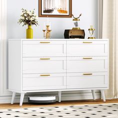 a white dresser with gold handles in front of a mirror and vases on top