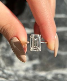 a woman's hand holding an engagement ring with a diamond in the middle and two fingers on it