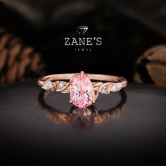 Introducing our stunning 14K Gold Floral Branch Pink Sapphire Ring, featuring a mesmerizing 1ct pink sapphire as the centerpiece.  This pear-cut gem is flanked by high-quality moissanite stones, with additional moissanite accents artfully set within the floral branch design of the band.  We recommend the rose gold setting, which beautifully complements the vibrant pink of the sapphire. This ring is an original design, meticulously handcrafted to ensure each piece is unique.  Available in a varie Pink Morganite Pear-shaped Jewelry, Pink Pear-shaped Cubic Zirconia Ring, Pink Pear-shaped Diamond Ring, Pink Pear-shaped Morganite Jewelry, Pink Pear-shaped Diamond Promise Ring, Pink Sapphire Jewelry With Center Stone, Pink Sapphire Ring With Diamond Accents For Promise, Pink Sapphire Promise Ring With Diamond Accents, Pink Sapphire Jewelry For Promise Ring