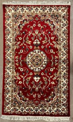 a red rug with an intricate design on the center and fringes hanging from it