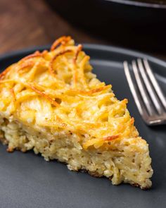 a slice of quiche on a black plate with a fork and bowl in the background