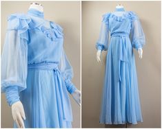 This is a frilly sky blue poly chiffon 70s maxi dress. It has a high neck collar that is ruched and a sheer neckline with a ruffle that sweeps over the bust and shoulders. It has long bishop-style sleeves and ruched cuffs that button. The top has a blousy fit and there is elastic at the waistline and a sash belt to cinch in the waist. The skirt is a loose flowy A-line skirt that falls to the floor. The dress zips up the back with a nylon zipper and a keyhole detail to the collar that fastens with buttons. The dress is fully lined in a sky-blue acetate.  Condition: The dress is in good condition with a few small spots to note. On the front of the skirt lining there are a few little yellow spots. They are faint and they do not show with the chiffon overlay. There is also one small gray mark Blue Flowy Dress With Bell Sleeves, Light Blue Victorian Dress, Blue Billowy Dress With Puff Sleeves, Sheer Ruffle Dress, Vintage Blue Long Sleeve Maxi Dress, Victorian Blue Dresses With Ruffles, 70s Prom Dress, Blue Chiffon Maxi Dress, 70s Fashion Women