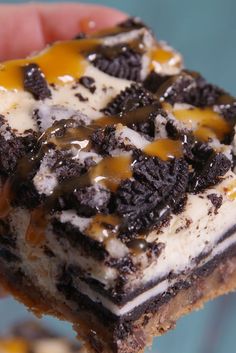 a hand holding a piece of cake with oreo cookies on it and caramel drizzle