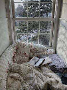 a bed sitting in front of a window next to a book on top of a pillow