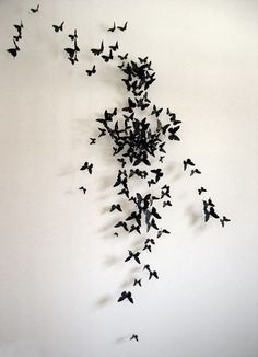 a flock of black birds flying in the air over a white wall with no one on it