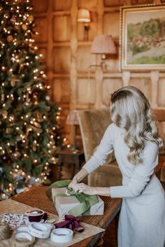 a woman in white dress standing next to a christmas tree with presents on the table