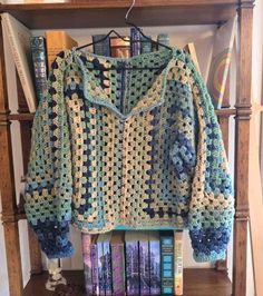 a crocheted sweater sitting on top of a book shelf next to a pile of books