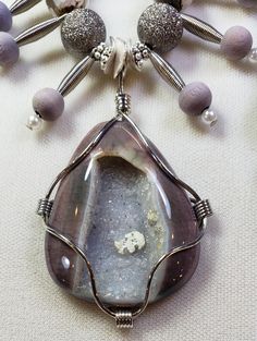 Gorgeous agate geode stone pendant with a simple yet strong wire wrapping. (The marking near the center of the geode is part of the stone) I gave this pendant a necklace of dark gray silver textured beads (they have a little bit of sparkle to them and are lovely), faceted, variegated agate stone beads and vintage wood, wire and faux white pearl dangle charms. The silver spacers and toggle clasp are pewter (cadmium and lead free). This necklace is 21 inches long. The pendant has an approximate 2. Wire Wrapped Teardrop Agate Jewelry, Teardrop Agate Wire Wrapped Jewelry, Wire Wrapped Agate Pendant Jewelry, Hand Wrapped Agate Pendant Jewelry, Spiritual Agate Round Pendant Crystal Necklace, Spiritual Agate Crystal Necklace With Round Pendant, Adjustable Agate Jewelry With Large Pendant, Agate Round Pendant Necklace For Healing, Agate Round Pendant Crystal Necklace For Healing