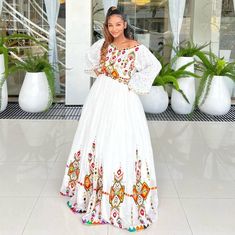 a woman standing in front of a building wearing a white dress with colorful designs on it