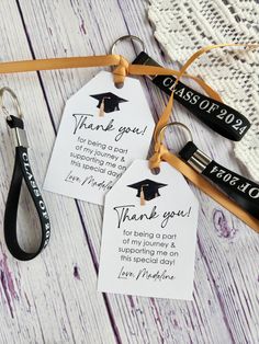 graduation thank you tags and lanyards on a white wooden table with black ribbon