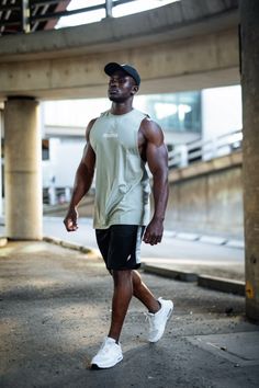 a man is walking down the street in shorts and a baseball cap with his hand on his hip