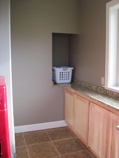 a laundry room with tile flooring and wooden cabinets in front of a window that has a basket on the counter