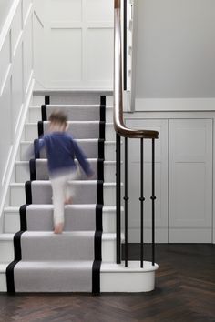 a little boy running down the stairs in a house with white walls and wood floors