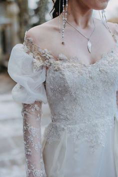 a woman in a white wedding dress with long sleeves and beaded necklaces on her neck