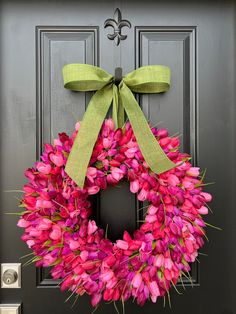 a pink wreath with a green bow hanging on a black front door, decorated with tulips