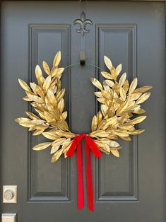 a wreath made out of gold leaves and red ribbon hangs on the front door of a house