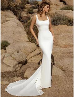 a woman standing in front of rocks wearing a long white dress with spaghetti straps and low back